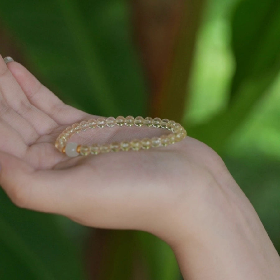 A hand holding a small citrine and jade bead bracelet against a green background