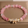 Close up of a pink cat's eye bead bracelet with a gold bow charm