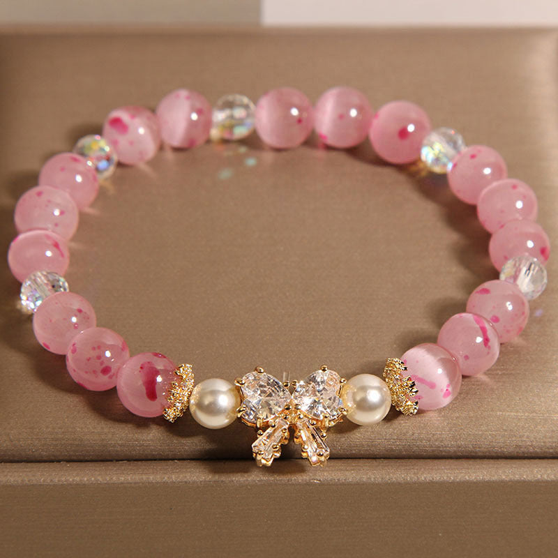 Close up of a pink cat's eye bead bracelet with a gold bow charm