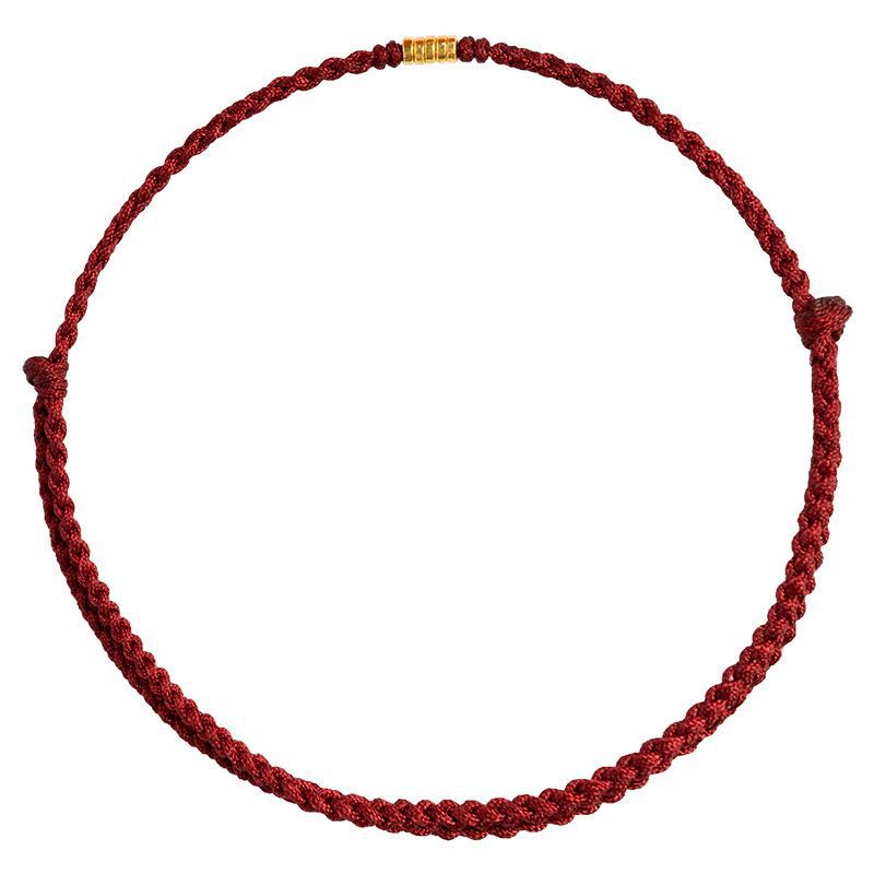 Close up of a braided red cord bracelet with a small gold bead on white background