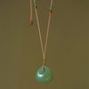 Close up of a smooth green jade lock pendant hanging on a brown cord
