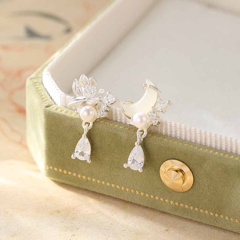Pair of silver lotus and moon earrings with pearls on a green box