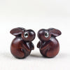 Close up of small carved wooden rabbit charms with inlaid eyes on a white surface