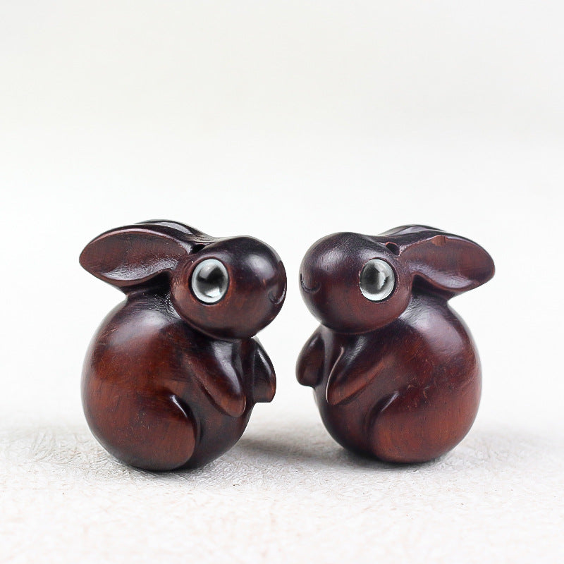 Close up of small carved wooden rabbit charms with inlaid eyes on a white surface