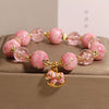 Close-up of a pink cherry blossom glass bead bracelet with a gold-tone rocking horse charm.