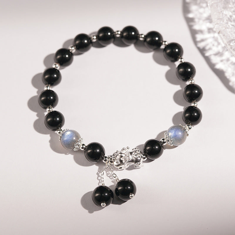 A black obsidian beaded bracelet with a silver Pixiu charm and dangling beads on a white background