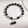 A black obsidian beaded bracelet with a silver Pixiu charm and dangling beads on a white background