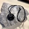 Polished black obsidian yin yang pendant on a black cord resting on a gray rock
