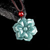 Close up of a carved blue green jade flower pendant on a brown cord