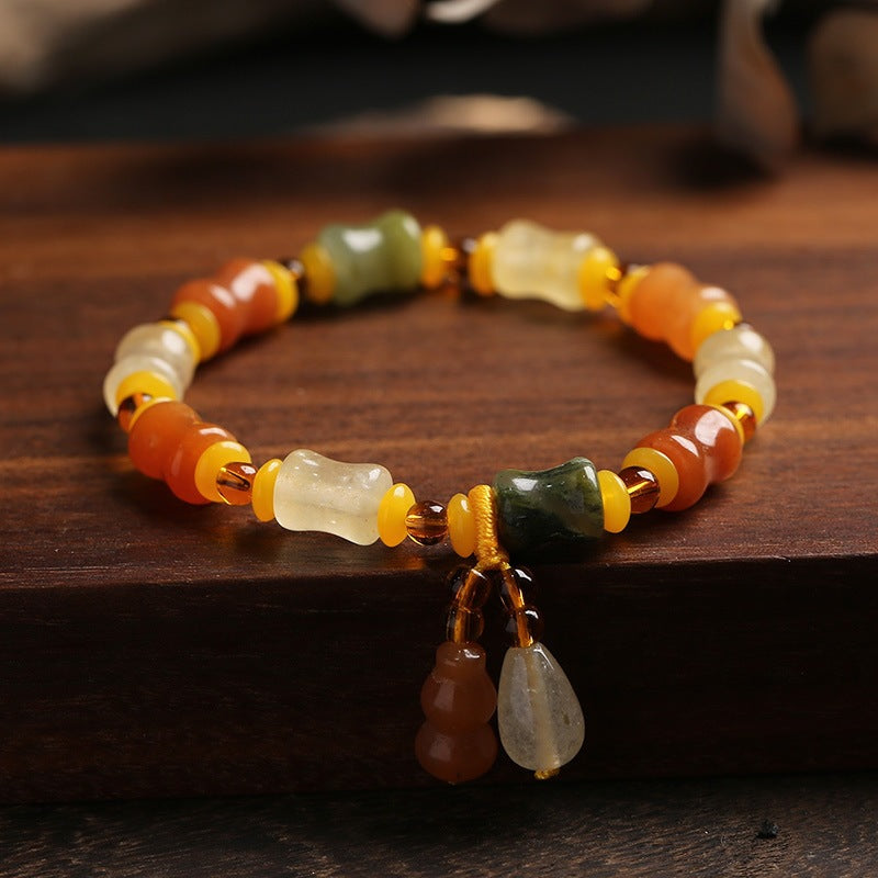 Hand-woven golden silk jade bracelet with gourd charm on wood