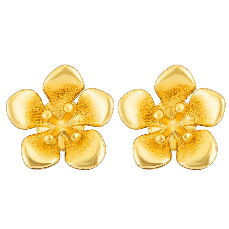 Pair of small gold-tone flower stud earrings made of sterling silver on a wooden surface