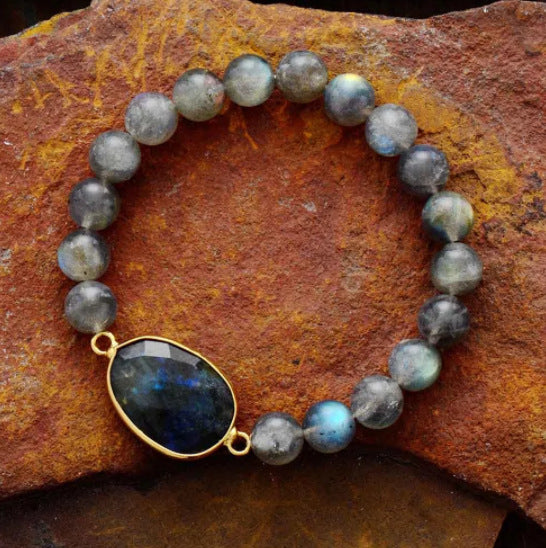 A beaded bracelet with a large oval stone centerpiece resting on a rock surface