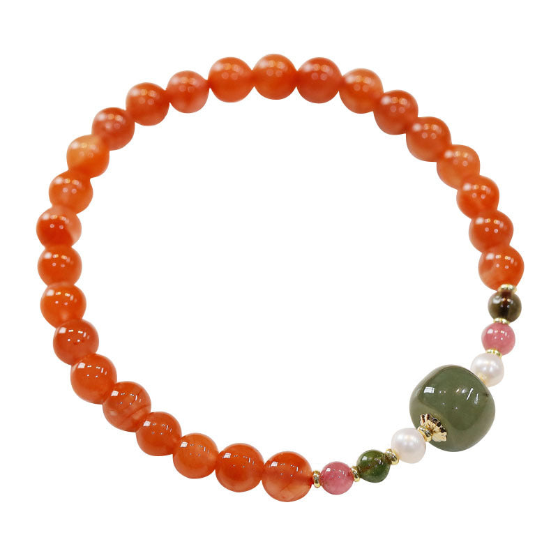 A beaded bracelet with red agate and a central green jade stone on a ceramic plate