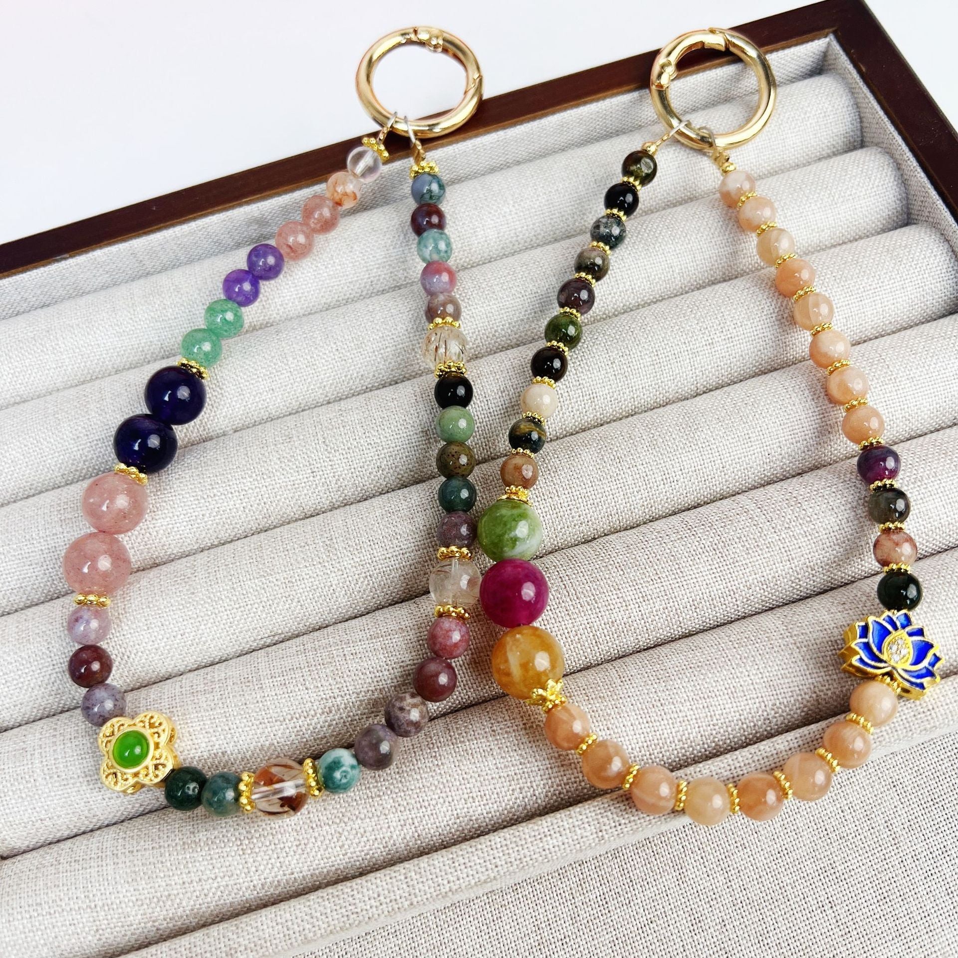 Two colorful beaded phone charms with gold rings on a white display tray