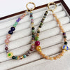 Two colorful beaded phone charms with gold rings on a white display tray