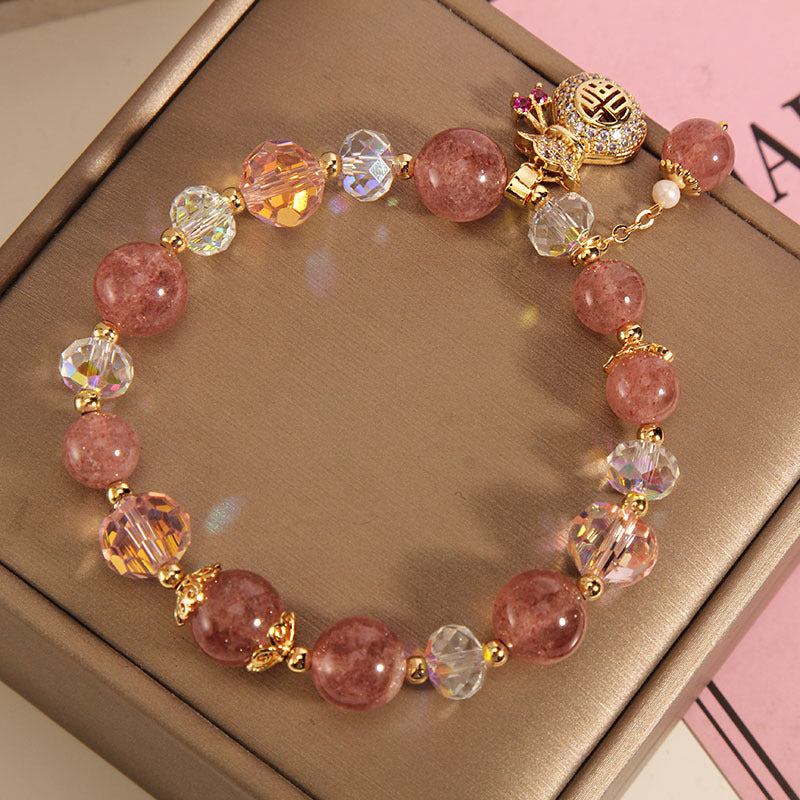 Pink strawberry quartz beaded bracelet with gold-tone money bag charm on a box