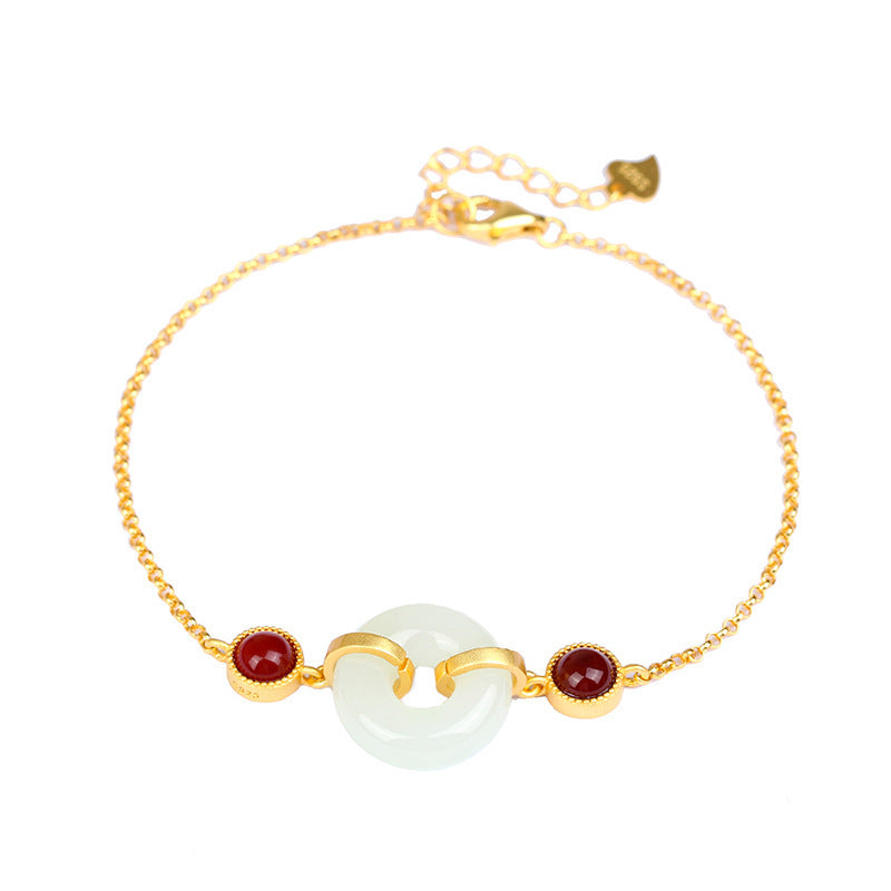 Close-up of a gold-tone bracelet with a white jade donut charm and red stones