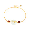 Close-up of a gold-tone bracelet with a white jade donut charm and red stones