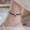 Close-up of a woman's ankle wearing a black braided anklet with a fox charm