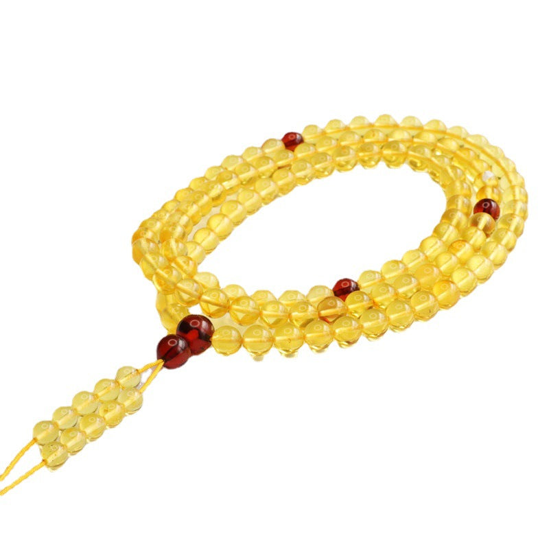 Coiled string of translucent yellow amber beads with red accents on a white background