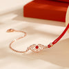 Close up of a Ruyi lock charm on a red cord and silver chain bracelet