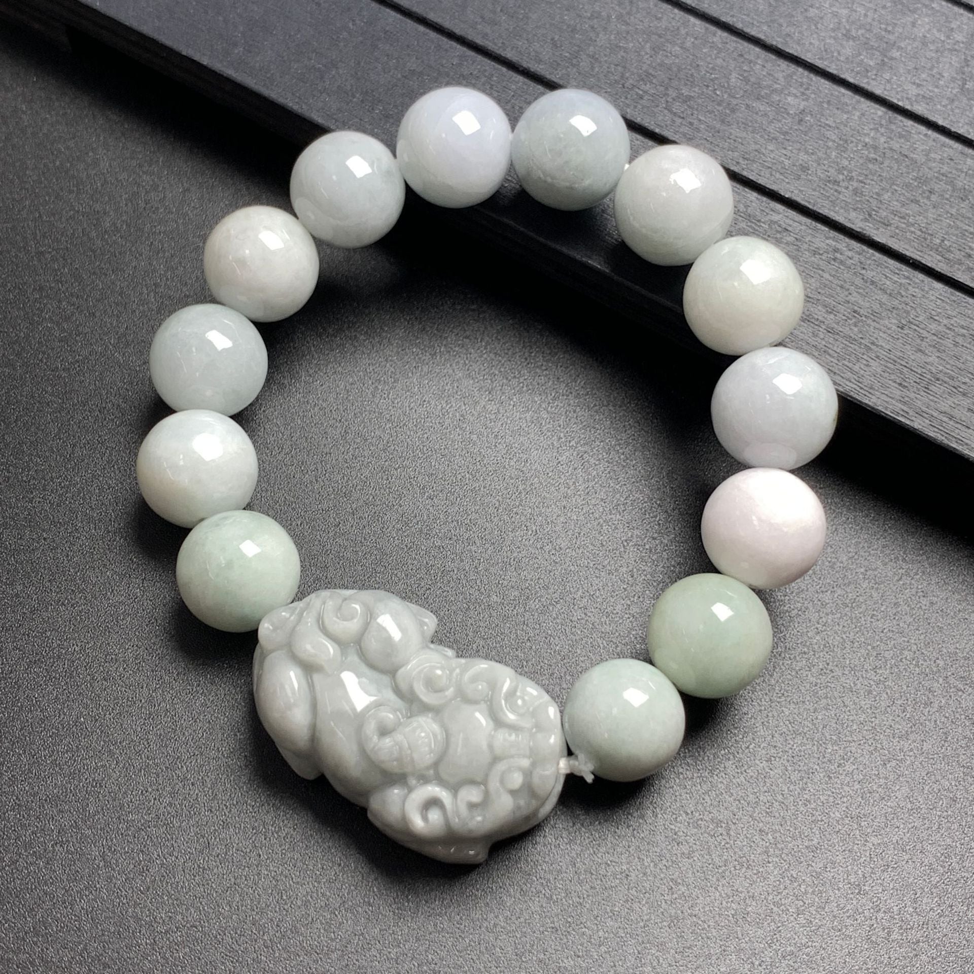 Close-up of a jade beaded bracelet with a carved Pixiu charm resting on a dark surface