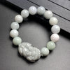 Close-up of a jade beaded bracelet with a carved Pixiu charm resting on a dark surface