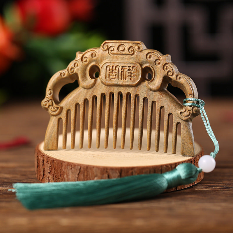 A carved wooden hair comb with a green tassel resting on a wooden slice.
