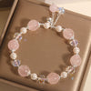 Pink crystal and pearl beaded bracelet with a dangling bell charm on a box