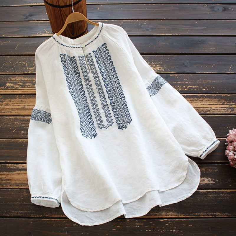 White long sleeve shirt with blue ethnic embroidery on a wooden background