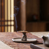 A ceramic incense burner shaped like a small meditating person holding an incense coil
