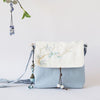 Light blue and white crossbody bag with floral embroidery and tassel details