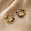Close-up of small gold-tone hoop earrings with green bamboo segments on a beige background