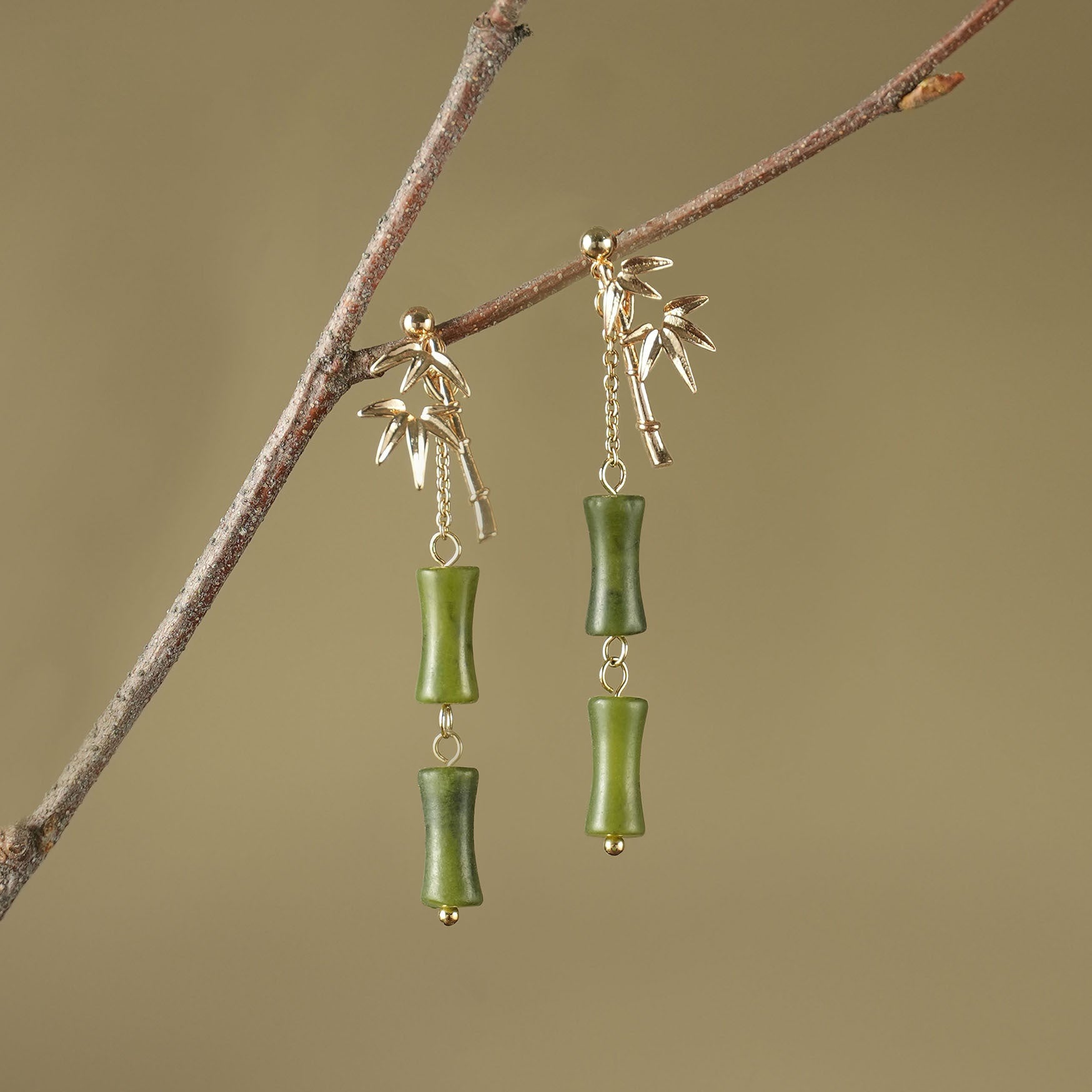 Gold tone bamboo leaf earrings with green peridot drops hanging from a branch