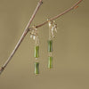 Gold tone bamboo leaf earrings with green peridot drops hanging from a branch
