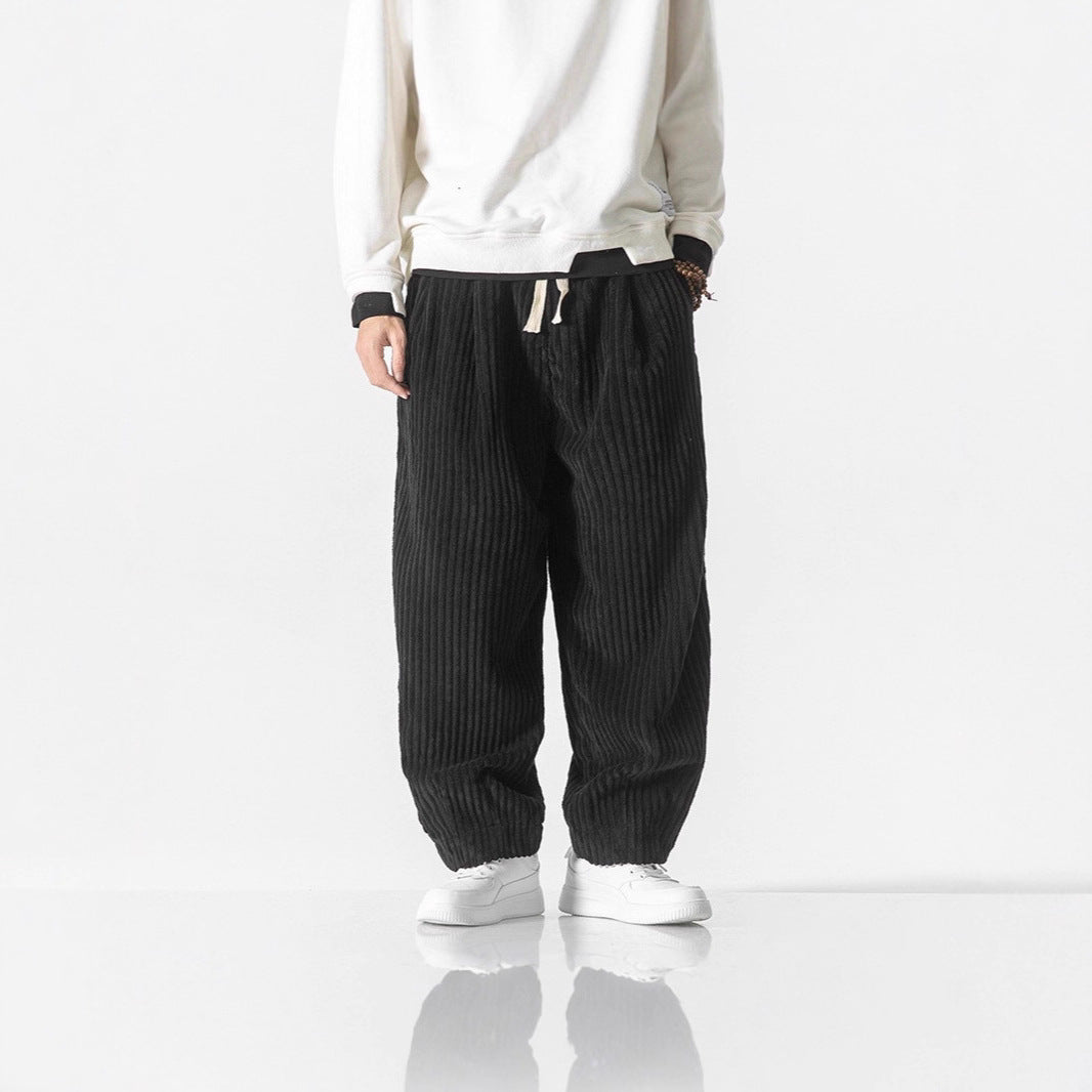 Full view of men wearing black corduroy harem pants with a drawstring waist