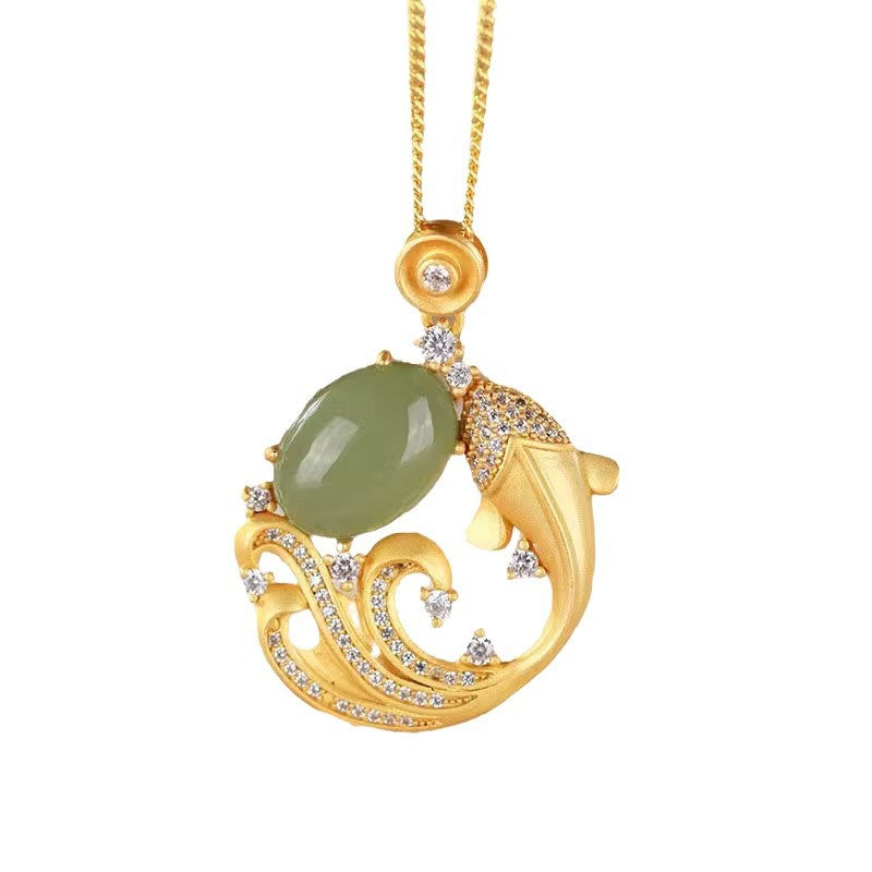 Gold-tone koi fish pendant with a smooth green stone resting on a soft jewelry box surface