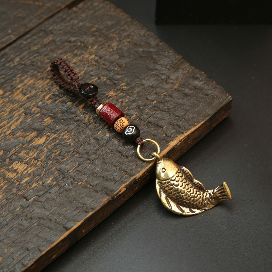 Close up of a brass koi fish keychain with red beads and a coin on a wooden surface