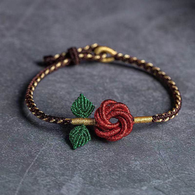 Close up of a woven cord bracelet with a red rose flower charm and green leaves