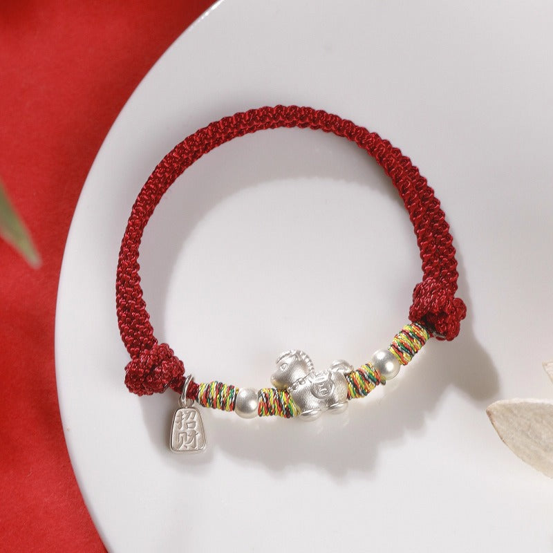 Close up of a woven red string bracelet with a silver horse charm on a wrist