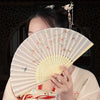A woman holding an open folding fan with a light background featuring small birds and pink flowers