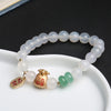 White agate beaded bracelet with gold money bag charm on a white dish