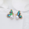 Gold tone butterfly stud earrings with iridescent abalone shell wings and white pearl drops on a white background