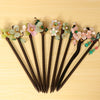 A row of dark wooden hairpins with colorful flower tops and beads lying on a light wood surface