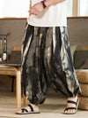 Man wearing loose black and white ink gradient harem pants sitting on a woven cushion