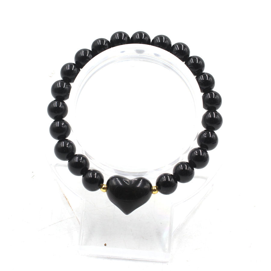A beaded bracelet made of black obsidian stones with a central heart-shaped charm on a display stand