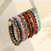 A collection of colorful natural stone beaded bracelets displayed on a stand