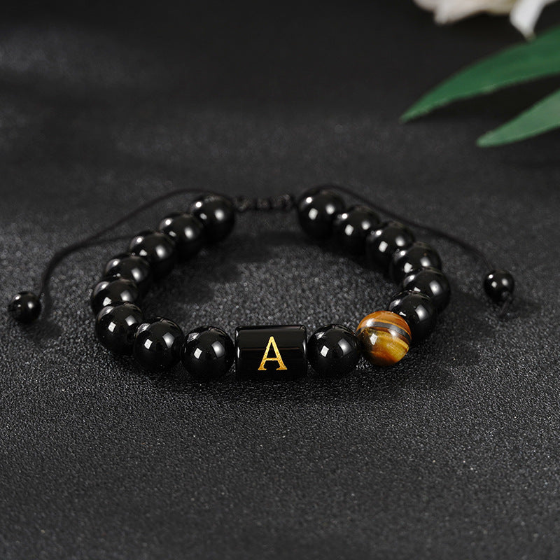 Black glass bead bracelet with a gold letter K and a tiger eye stone on a dark surface