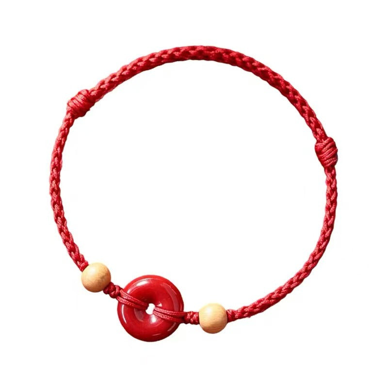 Close up of a red braided cord bracelet with a central red donut charm and two light wood beads