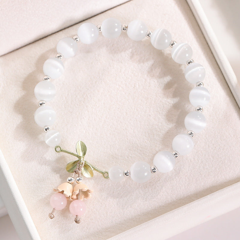 Close up of white cat's eye beads with a gold flower charm and pink crystal dangles